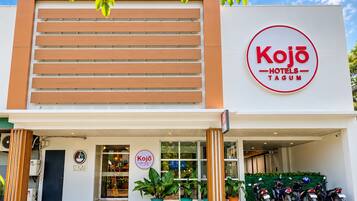 A hotel named Kojo Hotels- Tagum with a modern facade, a visible entrance, and a parking area with motorcycles.