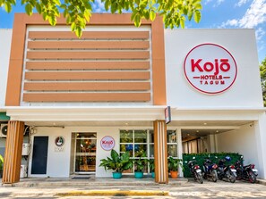 A hotel named Kojo Hotels- Tagum with a modern facade, a visible entrance, and a parking area with motorcycles.
