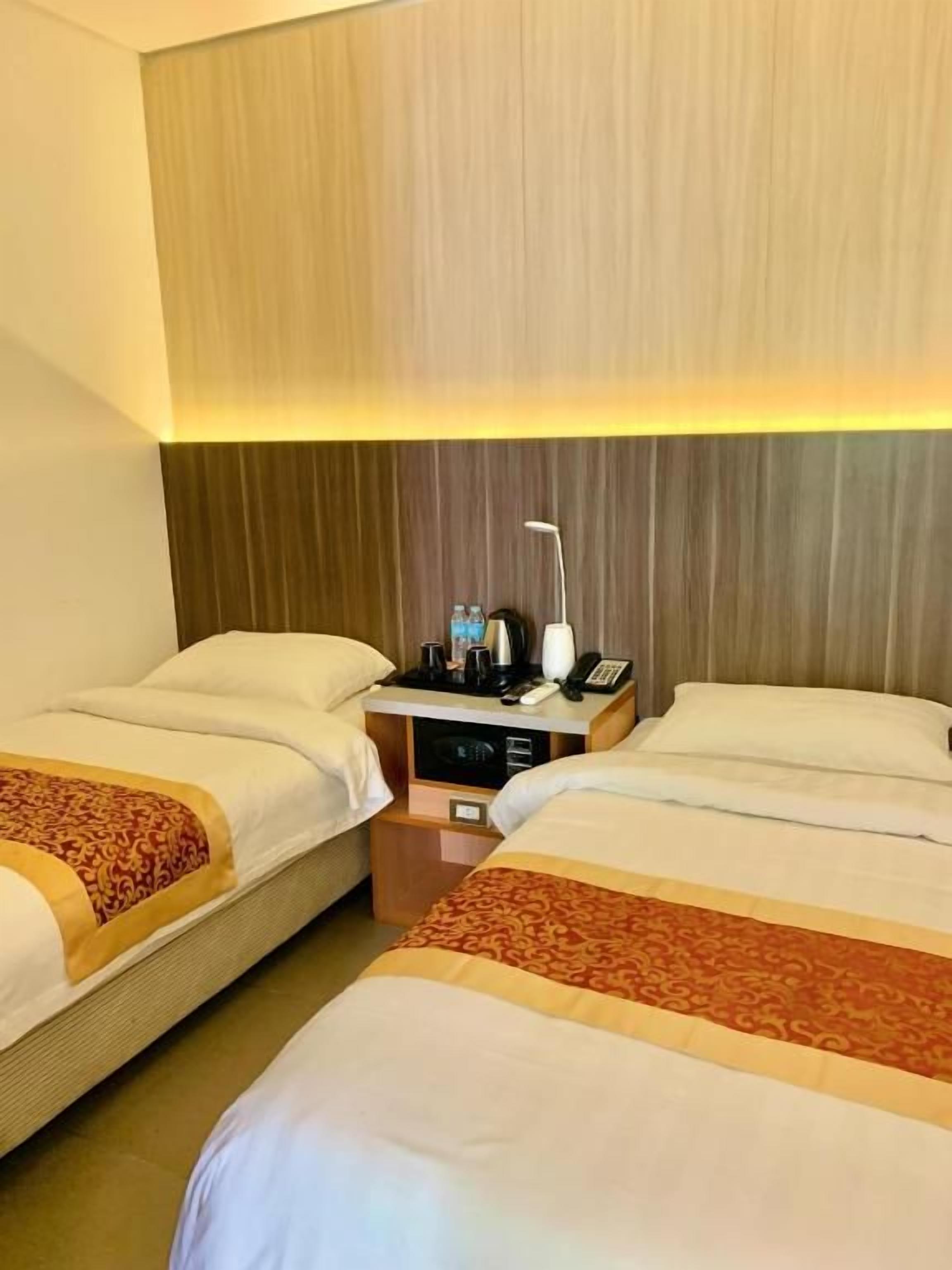 Hotellihuone, jossa on kaksi sänkyä, yöpöytä lampulla ja seinälle asennettu puhelin.