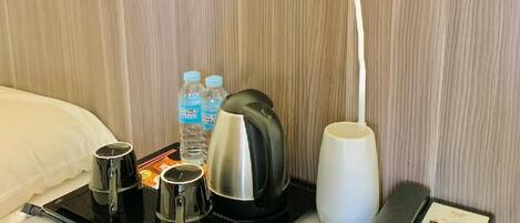 Una habitación de hotel con una cama, una mesita de noche con hervidor, cafetera, botella de agua, control remoto y teléfono.