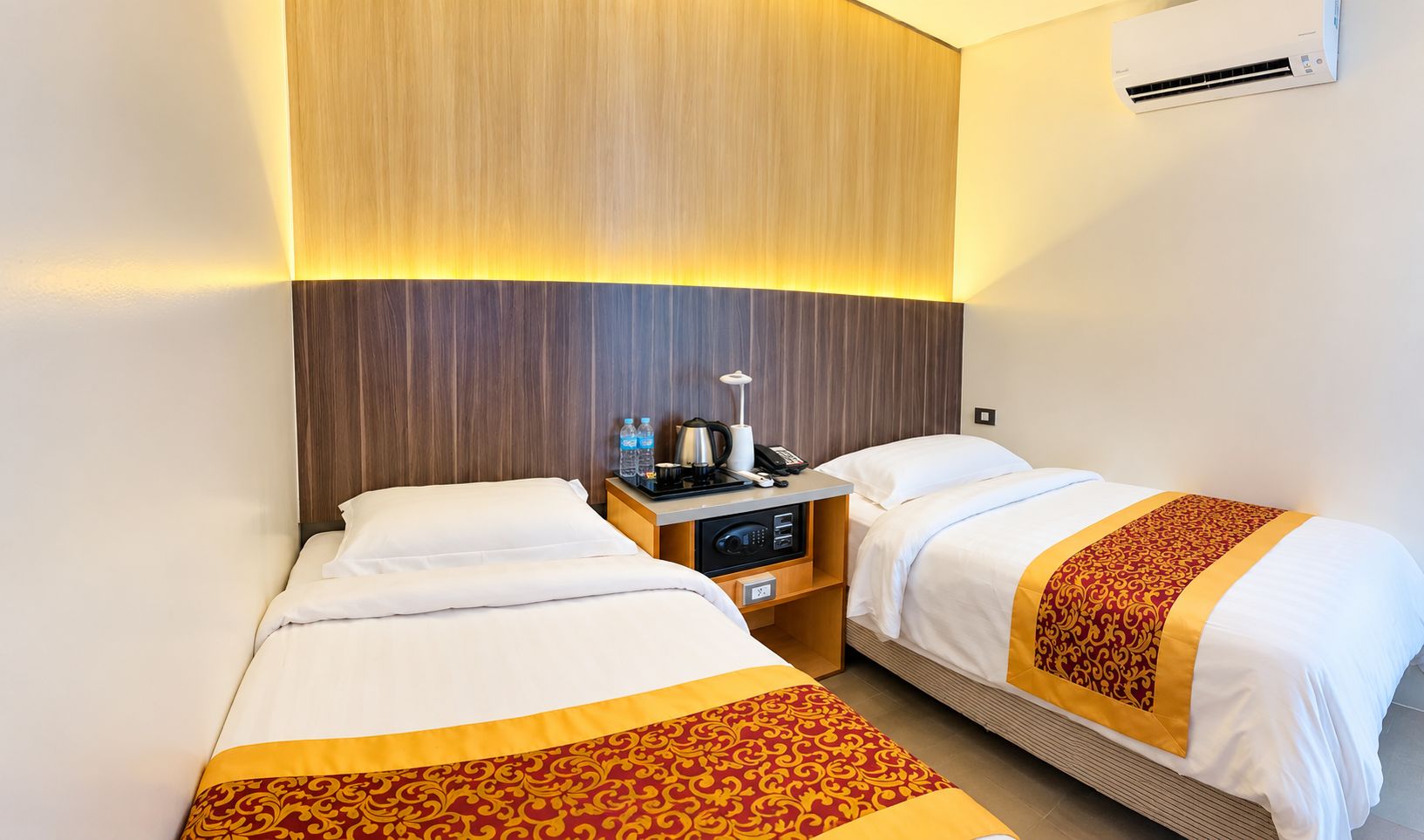 Habitación de hotel con dos camas, una mesita de noche con lámpara, una cafetera y un teléfono.