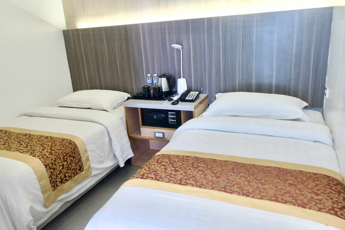 Habitación de hotel con dos camas, una mesita de noche con teléfono, lámpara y microondas.