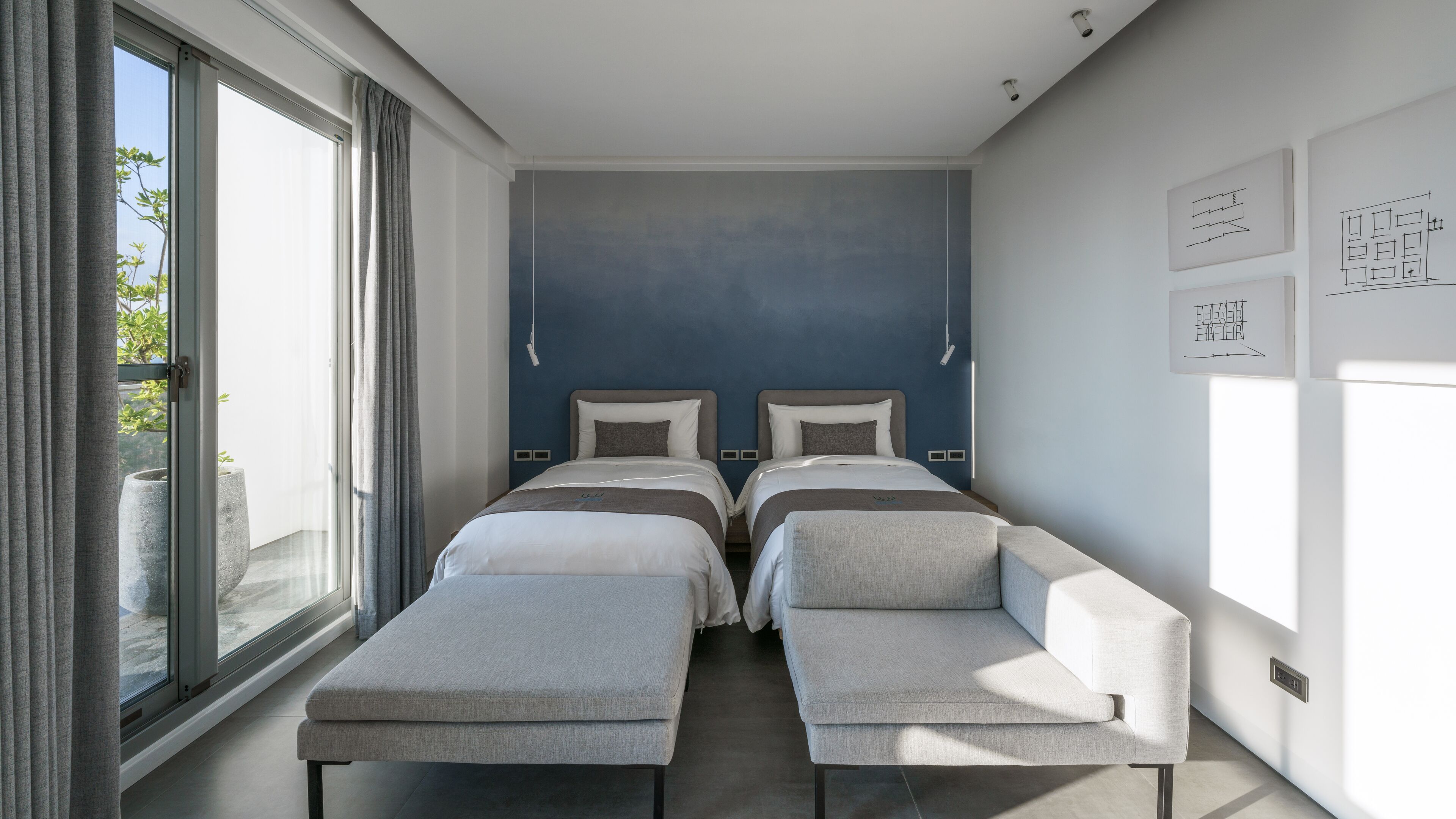 A modern hotel room with two beds, a bench, and a large window.