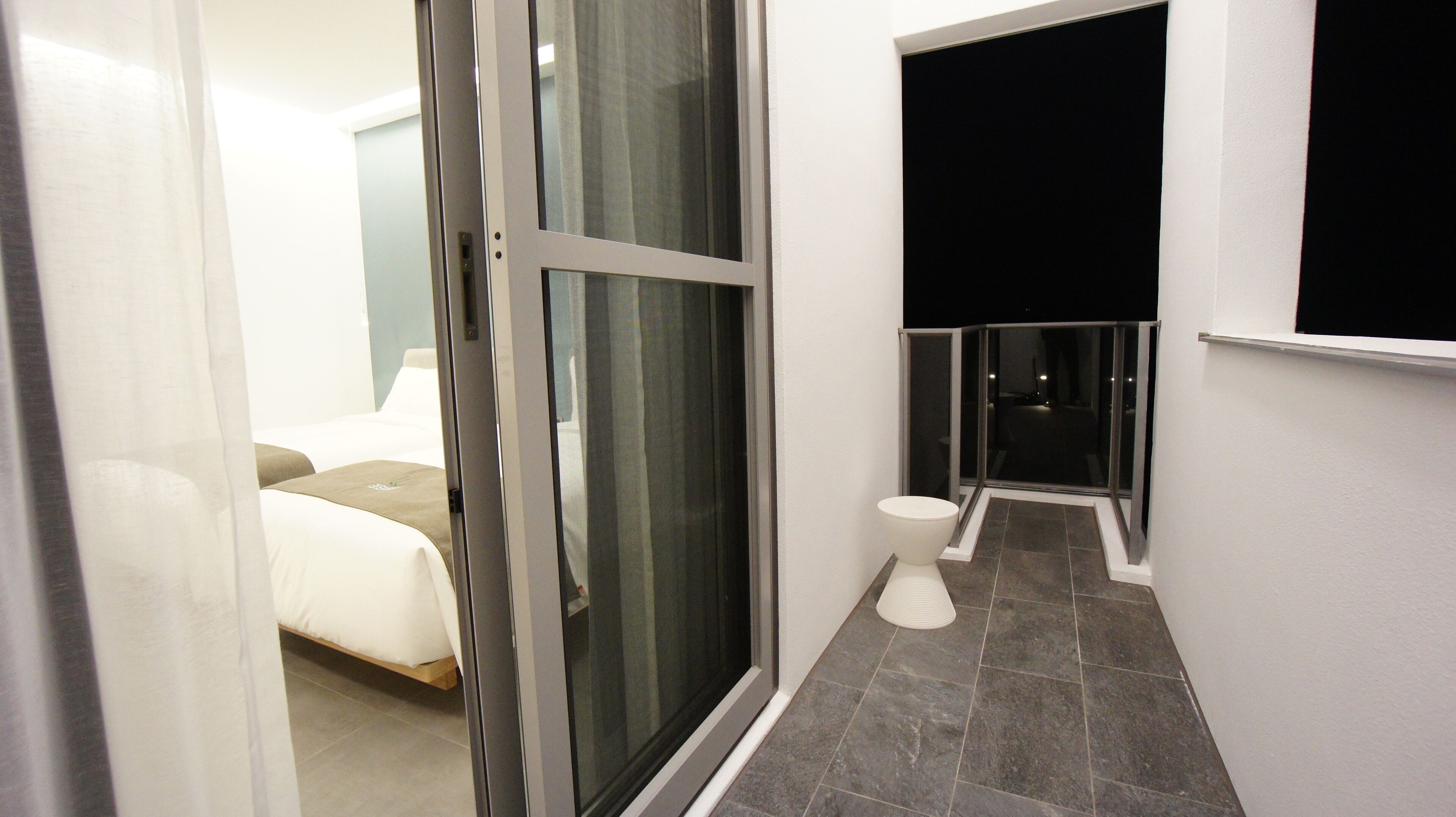 Ein modernes Hotelzimmer mit Bett, einem Badezimmer mit Toilette und Dusche sowie einer Glastür, die auf einen Balkon führt.
