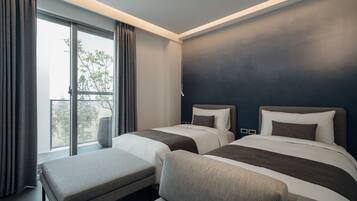 Ein modernes Hotelzimmer mit zwei Betten, einem großen Fenster inklusive Vorhängen, einer Bank und Blick auf Bäume.