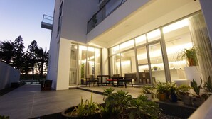 Un edificio moderno con grandes puertas de vidrio que dan a un interior bien iluminado. Varias plantas en macetas están en primer plano, y el edificio presenta un diseño contemporáneo y limpio.