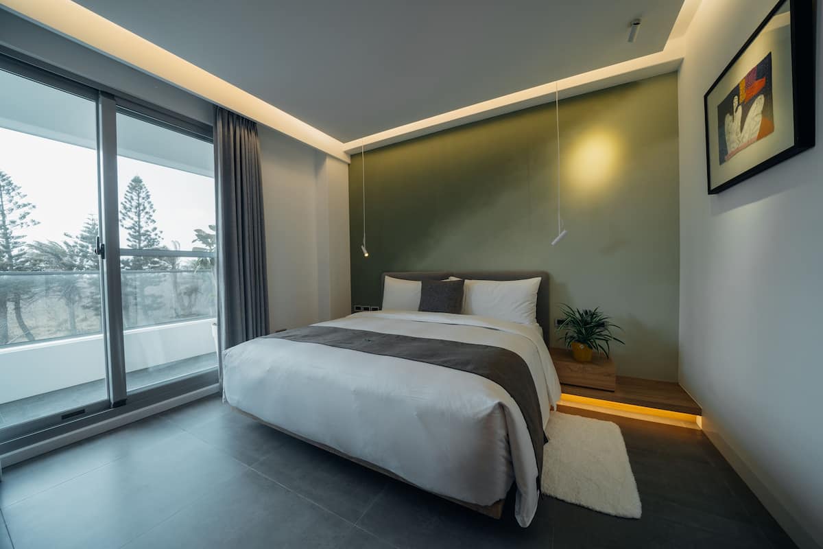 A modern bedroom with a large bed, a view through a sliding door, and a painting on the wall.