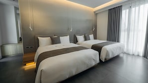 Una habitación de hotel moderna con dos camas, un ventanal con cortinas y un diseño minimalista.