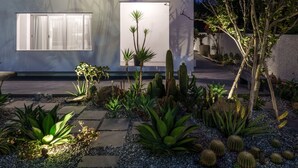 Un edificio moderno de varios pisos con balcones, ventanas amplias y un jardín bien cuidado con cactus y otras plantas.