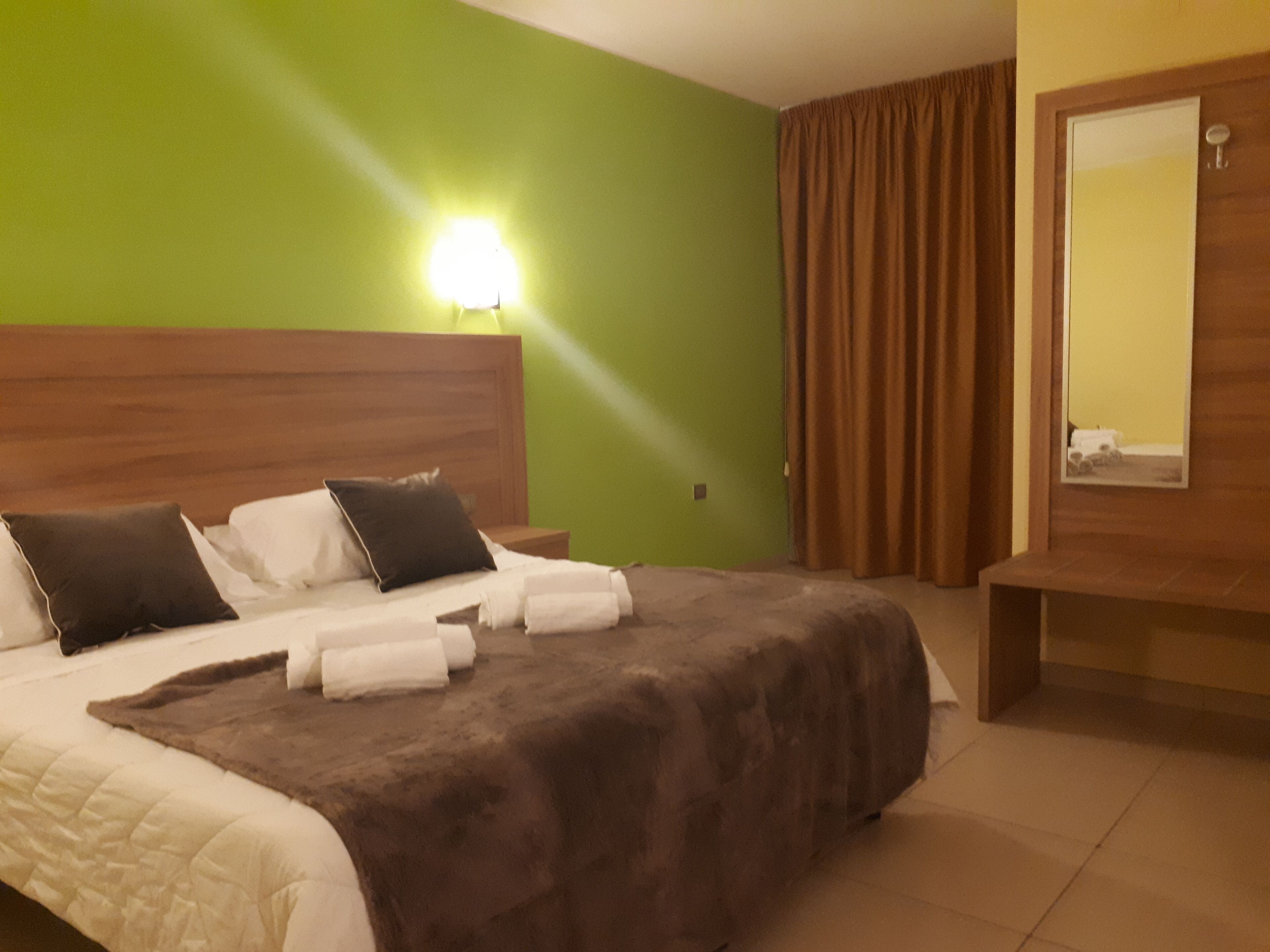 A hotel room with a bed, a nightstand, a mirror, and a green wall.