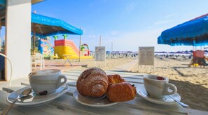 Un café frente a la playa con una mesa para dos, con croissants y tazas de café.