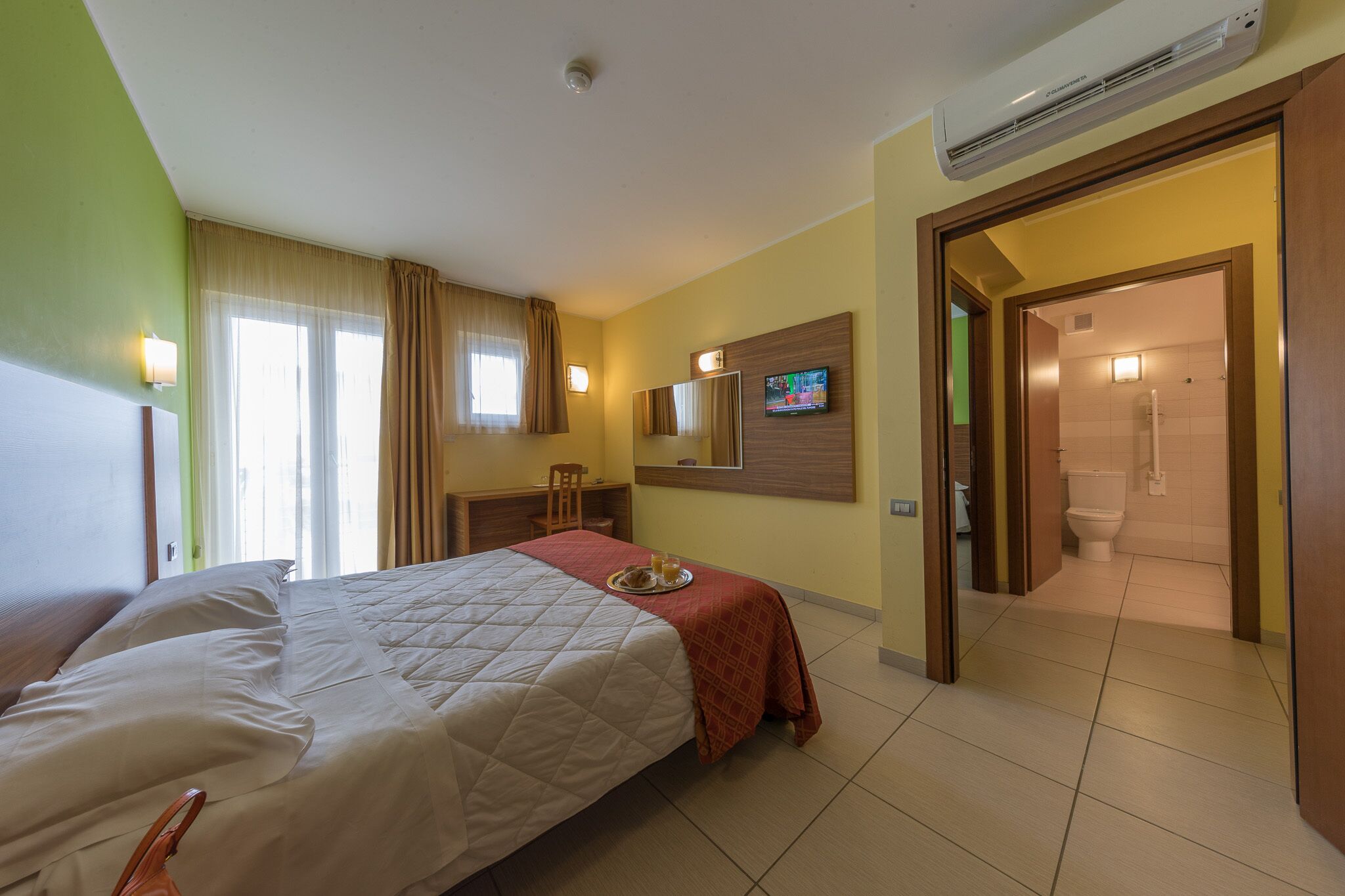 Camera d'albergo con un letto, una scrivania, una sedia, una televisione e un bagno visibile attraverso una porta aperta.