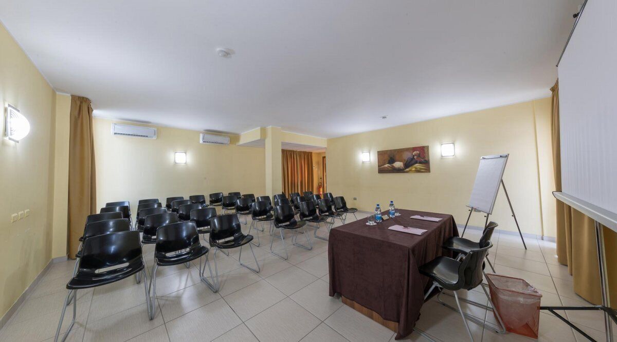 A conference room with rows of chairs, a table with a brown tablecloth, a whiteboard, and an air conditioning unit on the wall.