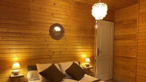 A cozy wooden room with a bed, two bedside lamps, a decorative mirror, and a door. - Welcome to Soleil, à la Neige, a pleasant family resort where life is good! (Eyne)