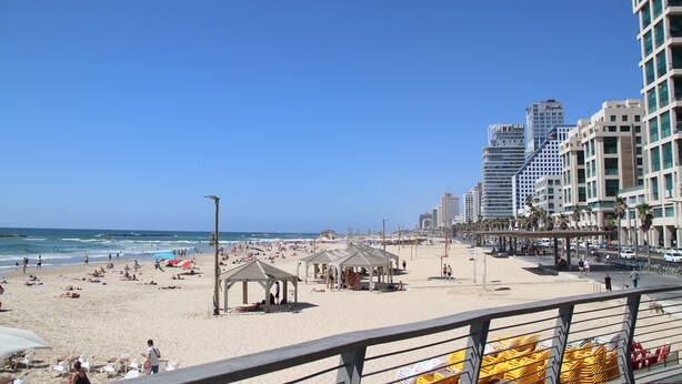 Une plage avec des parasols, des tentes et des gens. On aperçoit de grands immeubles à l’arrière-plan.