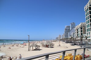 Una playa con sombrillas, carpas y gente. Se ven edificios altos al fondo.