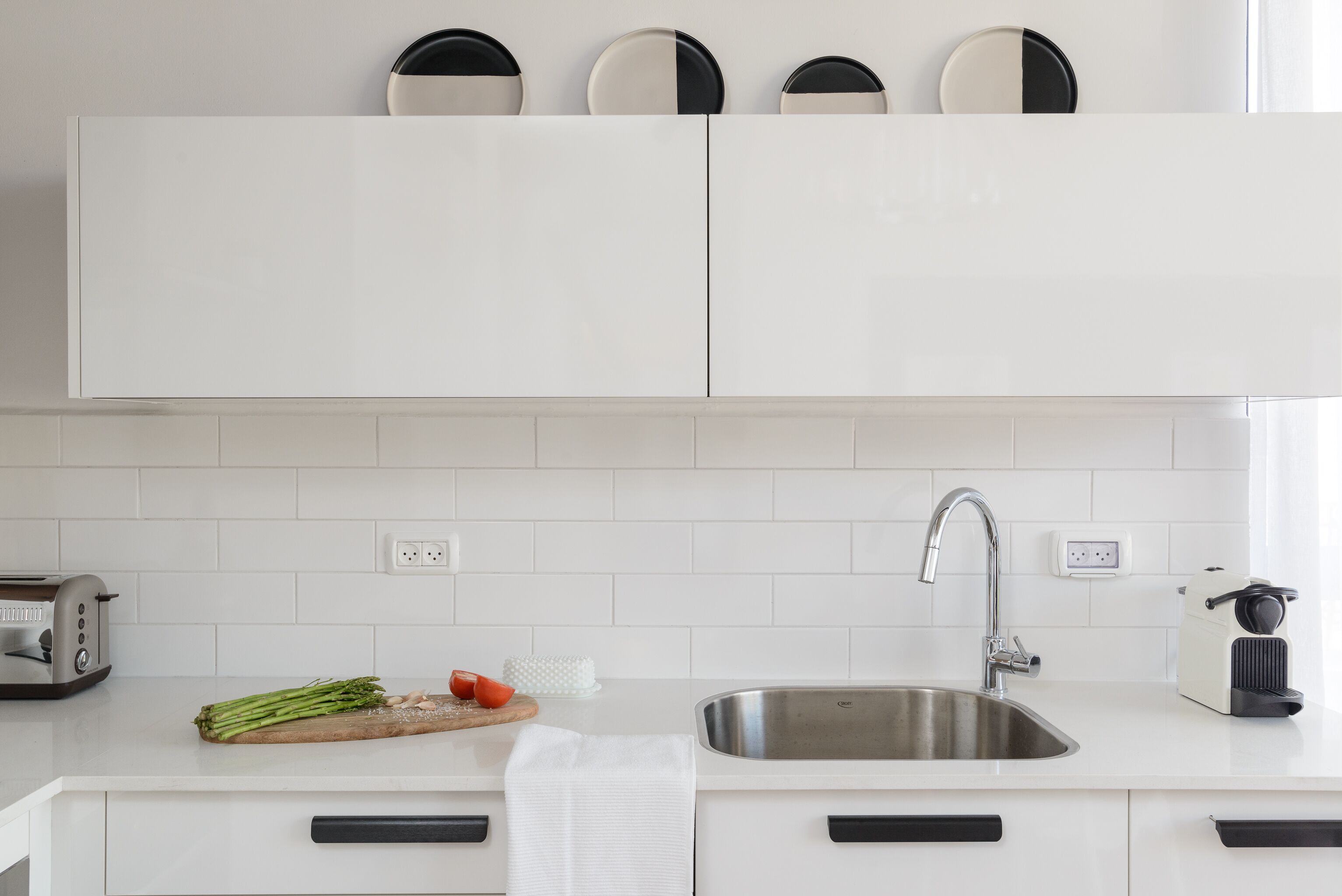 A modern kitchen with white cabinets, a stainless steel sink, a toaster, and fresh vegetables on the counter.
