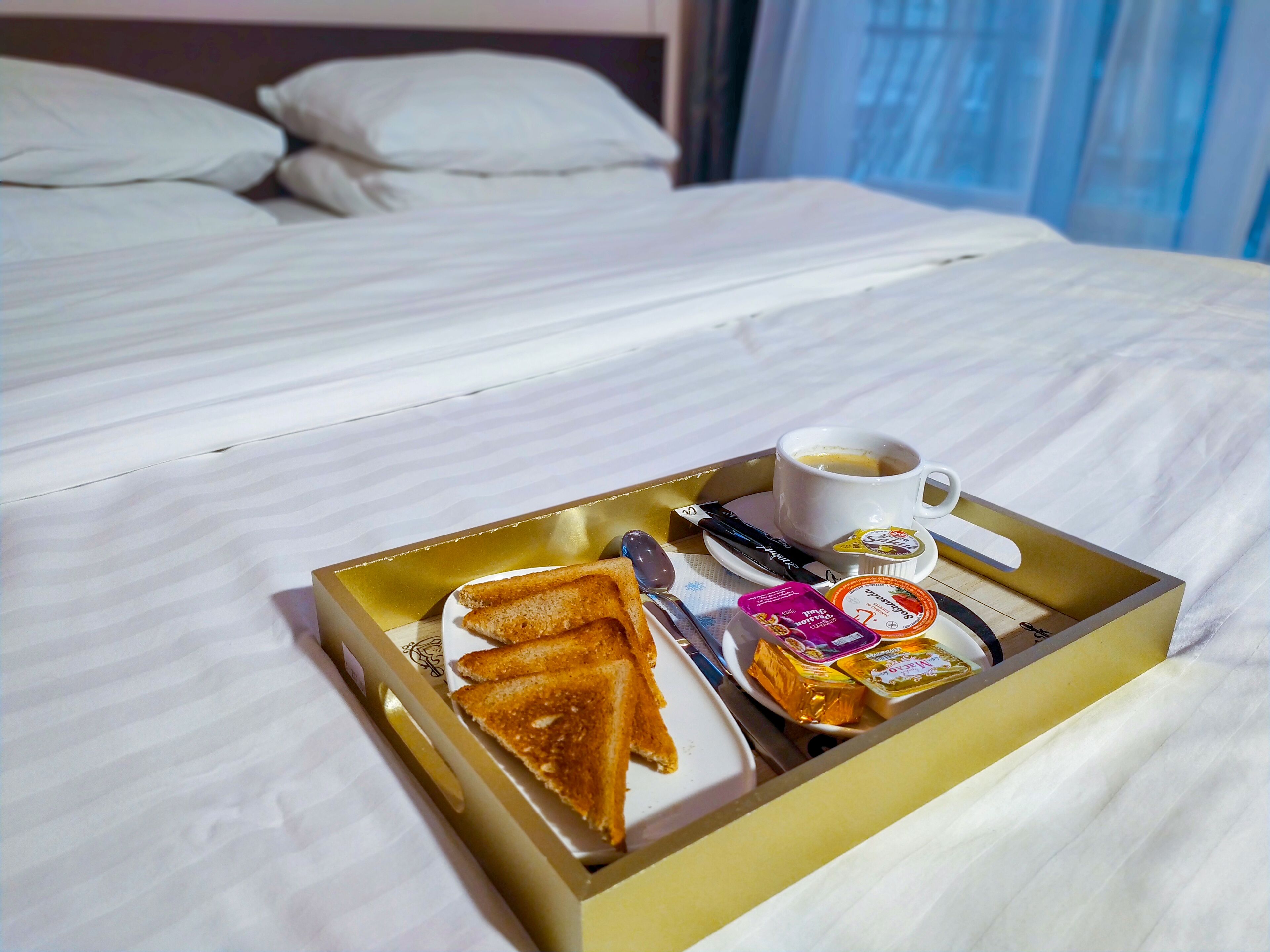 A breakfast tray on a bed with toast, a cup of coffee, and some spreads.
