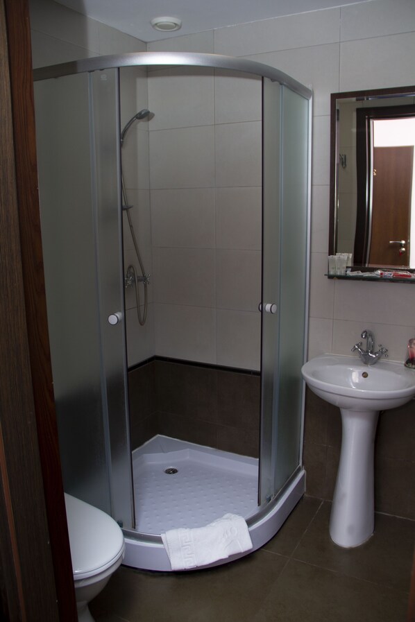 Un baño moderno con ducha de vidrio, lavamanos pedestal blanco y un inodoro.