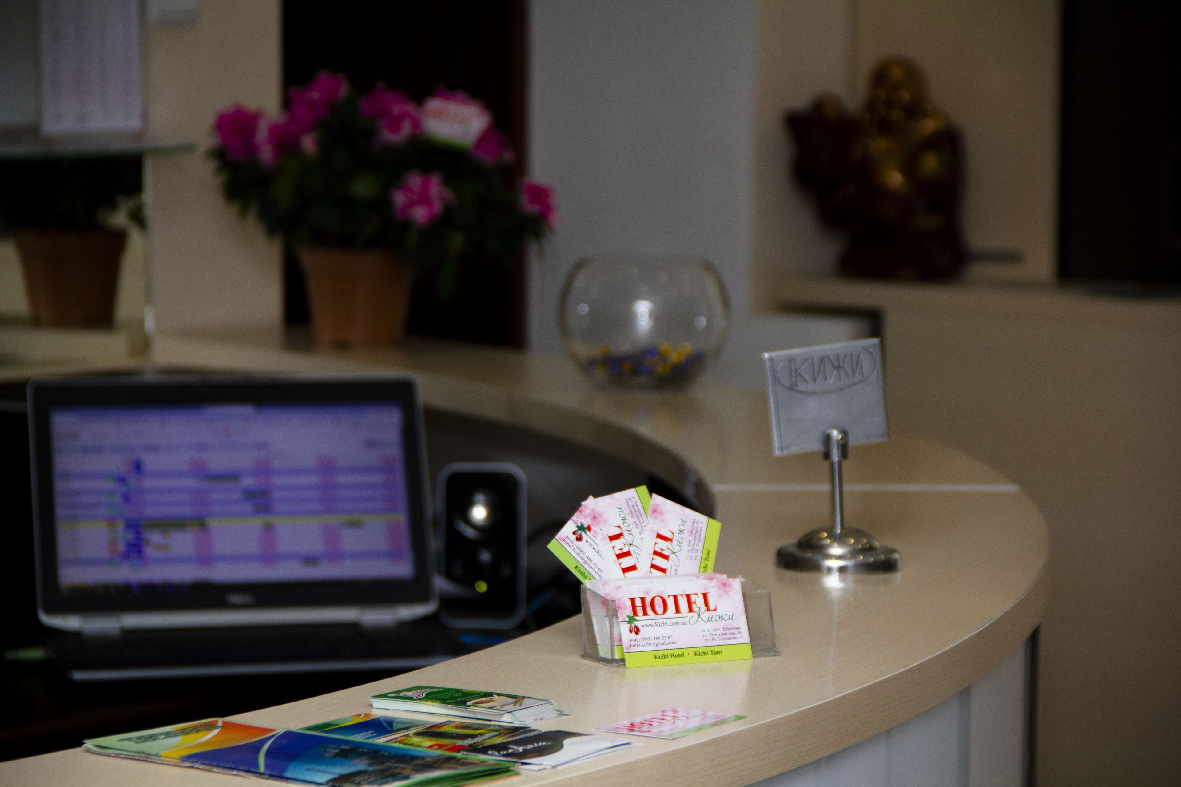 Mostrador de recepción de hotel con una computadora portátil mostrando un itinerario, un jarrón de flores y una pequeña estatua de Buda.