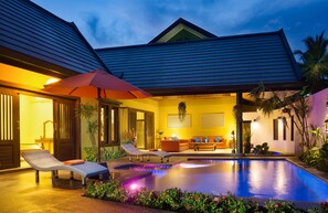 A poolside area with lounge chairs, a red umbrella, and a well-lit interior. - Villa Topaz (Koh Samui)
