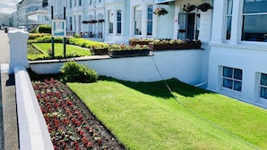 A white Four Oaks Hotel with a car park sign, surrounded by well-maintained gardens and a neatly trimmed lawn.