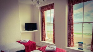 A hotel room with two beds, a TV, and large windows with curtains.