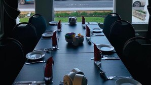 A dining table set for four with a view of parked cars and a body of water through large windows.