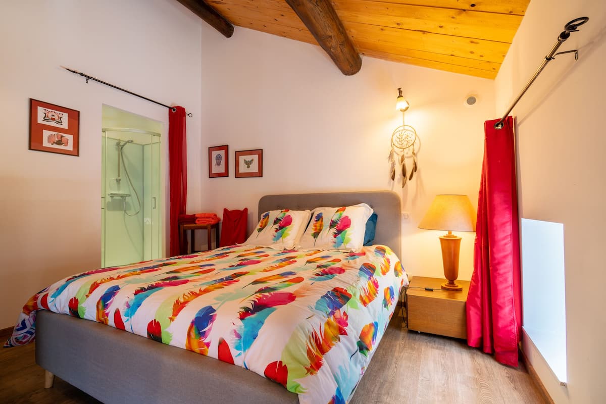 Une chambre à coucher avec un lit, une table de chevet avec une lampe, un attrape-rêves et un rideau rouge.