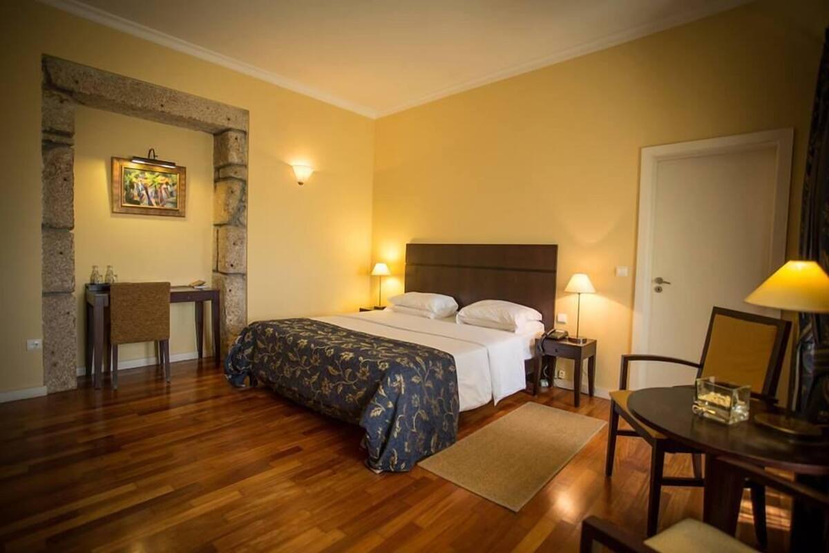 Une chambre d’hôtel avec un lit, un bureau, une chaise et une petite table avec une lampe.