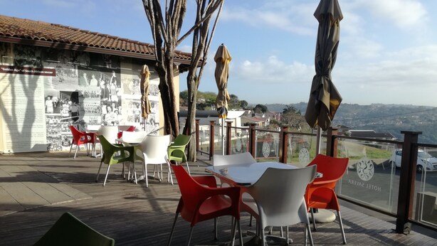 A terrace with tables and chairs, a wall with historical photos, and a view of the landscape. - Hotel Savera (Chatworth)