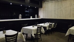 A restaurant with tables covered in white tablecloths and dark wooden chairs. A menu titled "The Ships that brought Indians to South America" is displayed on the wall. - Hotel Savera (Chatworth)