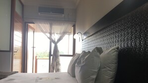 A bedroom with a bed, a window with sheer curtains, an air conditioning unit, and a textured wall. - Hotel Savera (Chatworth)
