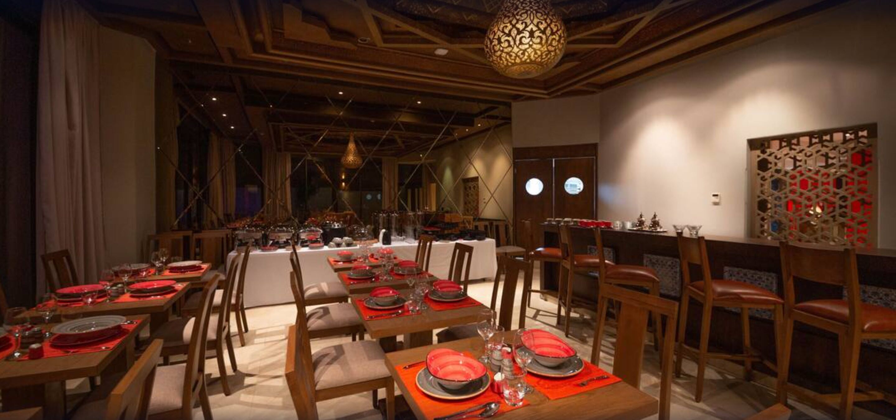 A dining area with multiple tables set for a meal, featuring a modern chandelier and a decorative wall piece.
