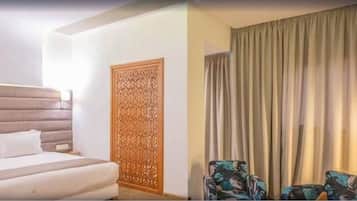 Habitación de hotel con cama, un panel de madera decorativo, dos sillones y un ventanal con cortinas.