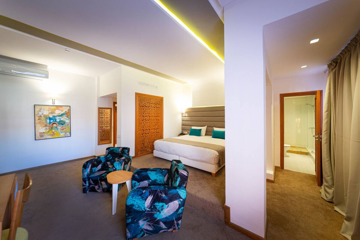 A hotel room with a bed, two armchairs, a small table, and a shower area.