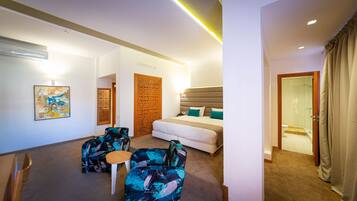 A hotel room with a bed, two armchairs, a small table, and a shower area.