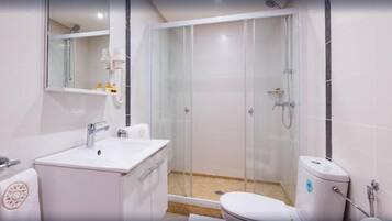 Un baño moderno con ducha de vidrio, lavamanos blanco y retrete.