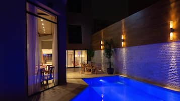 Un área de piscina al aire libre con pared de madera, asientos y una planta en maceta.