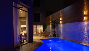 An outdoor pool area with a wooden wall, seating, and a potted plant.
