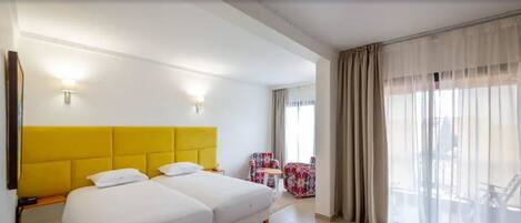 Een hotelkamer met een tweepersoonsbed, twee nachtkastjes, een stoel en een raam met gordijnen.