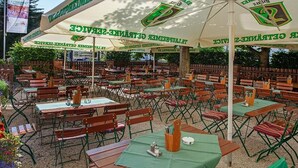 An outdoor seating area with tables and chairs under umbrellas, surrounded by greenery. - Brauerei-Gasthof-Hotel Laupheimer (Westerheim)