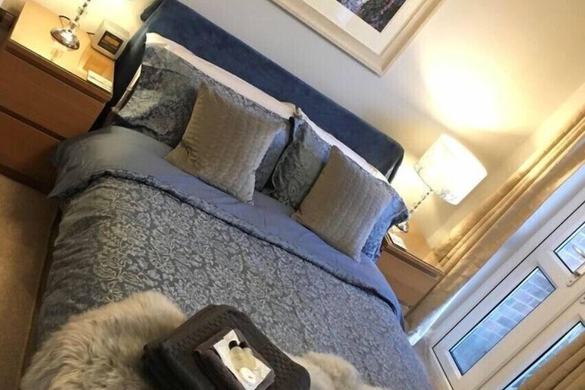 A neatly made bed with a fluffy gray blanket, a framed picture above the bed, and two bedside lamps.
