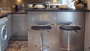 A modern kitchen with stainless steel appliances, a central island with bar stools, and pendant lighting. - Ourhaus (Beverley)