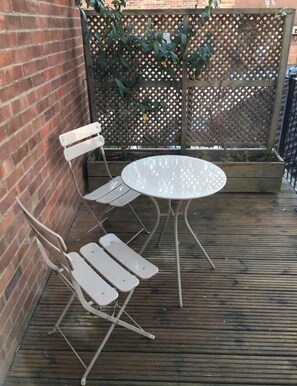 Un patio con una mesa redonda y dos sillas, una pared de ladrillo y una cerca de celosía.