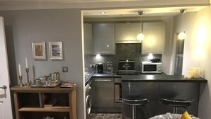A compact living space with a kitchenette, a dining area with a bar stool, and a bookshelf. - Ourhaus (Beverley)