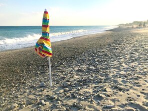 Une plage avec un parasol coloré planté dans le sable.