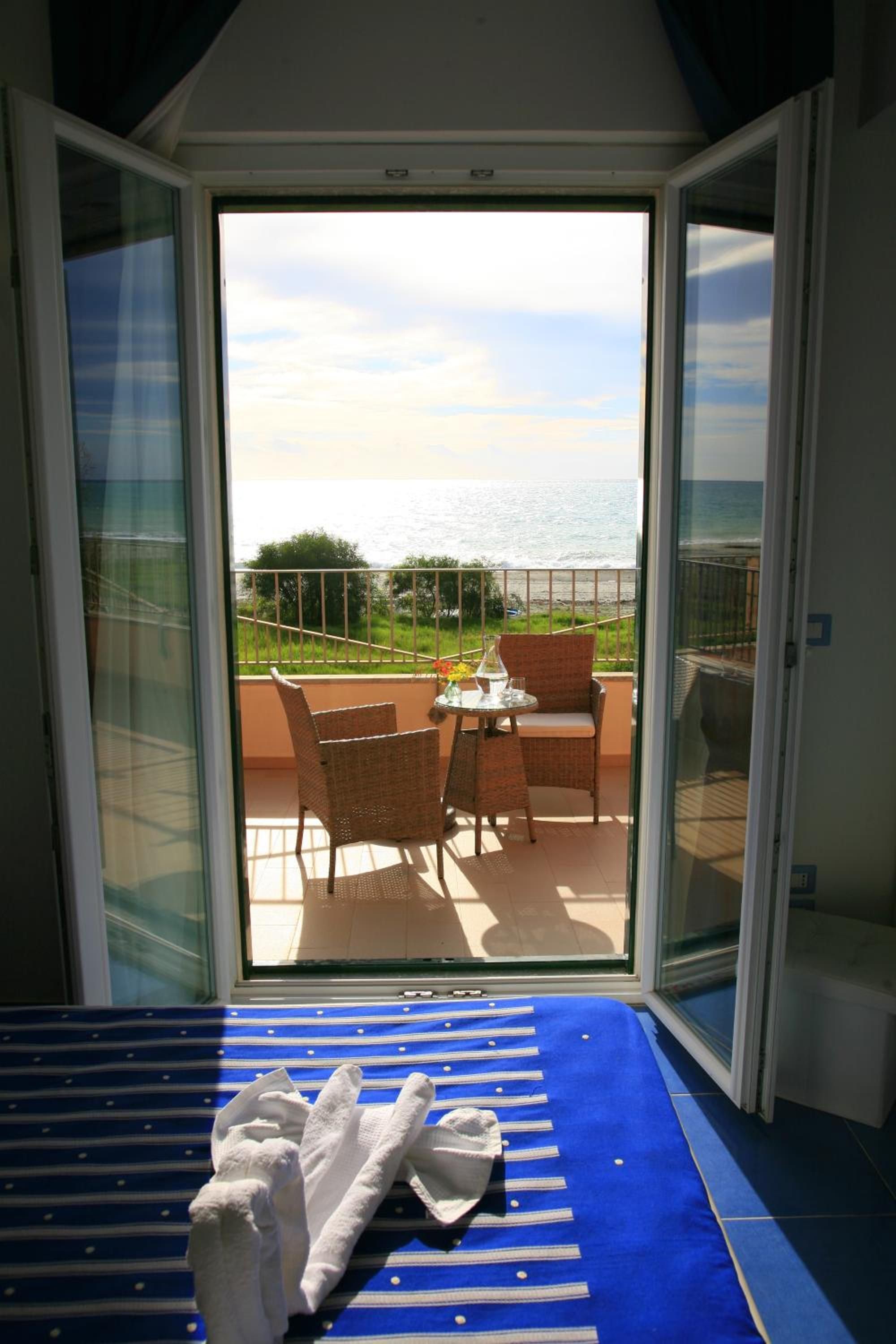 A room with a view of the sea through a sliding glass door, a bed with a blue-striped cover, and wicker furniture.