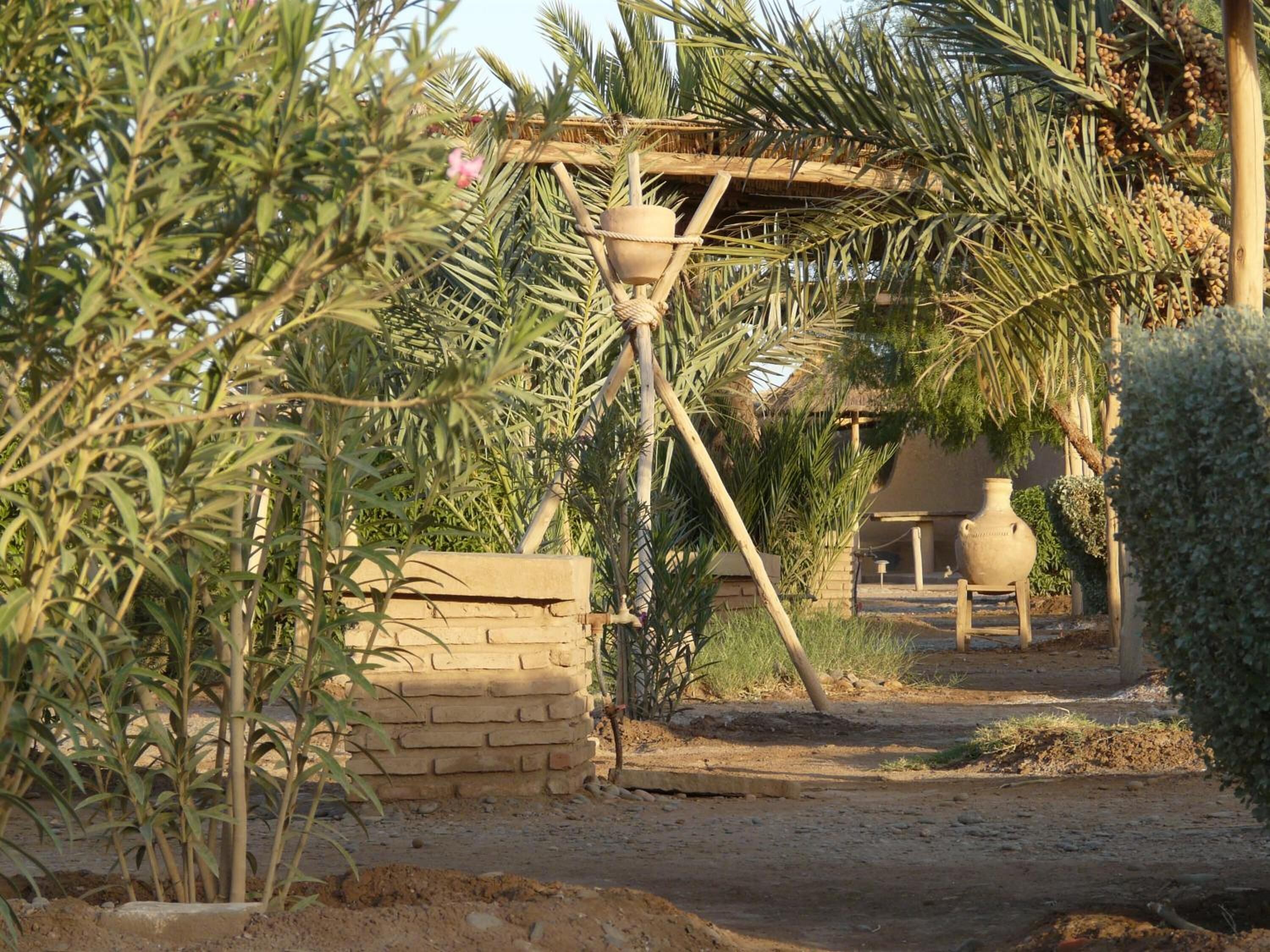 A rustic outdoor setting with a thatched-roof structure, a hanging pot, and a brick wall.