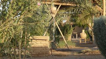 A rustic outdoor setting with a thatched-roof structure, a hanging pot, and a brick wall.